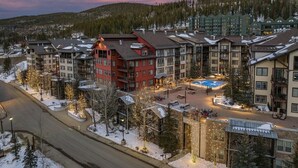 Un hotel de varios pisos con un patio central, rodeado de árboles cubiertos de nieve y un paisaje montañoso.