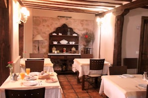 A dining area with tables set for meals, chairs, a wall-mounted shelf with dishes, and a lamp. - La Casona de Lucía (Siguenza)