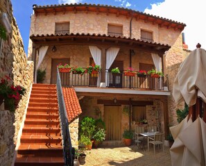 A two-story stone building with a balcony, a staircase leading to the entrance, and outdoor seating. - La Casona de Lucía (Siguenza)