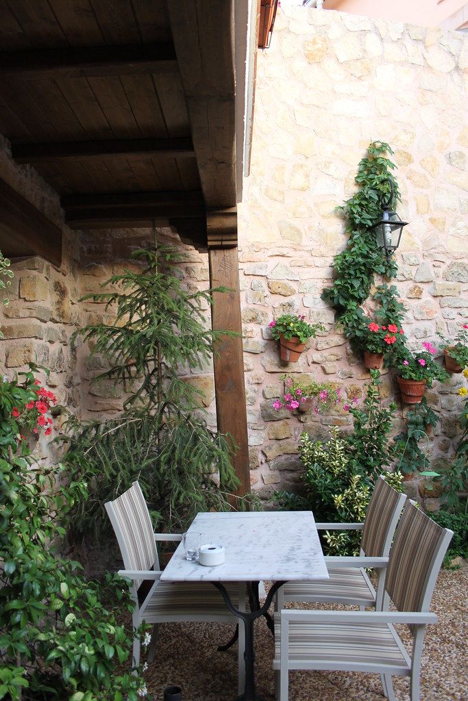 Mur de pedra amb plantes en testos i una taula amb caires a un pati.
