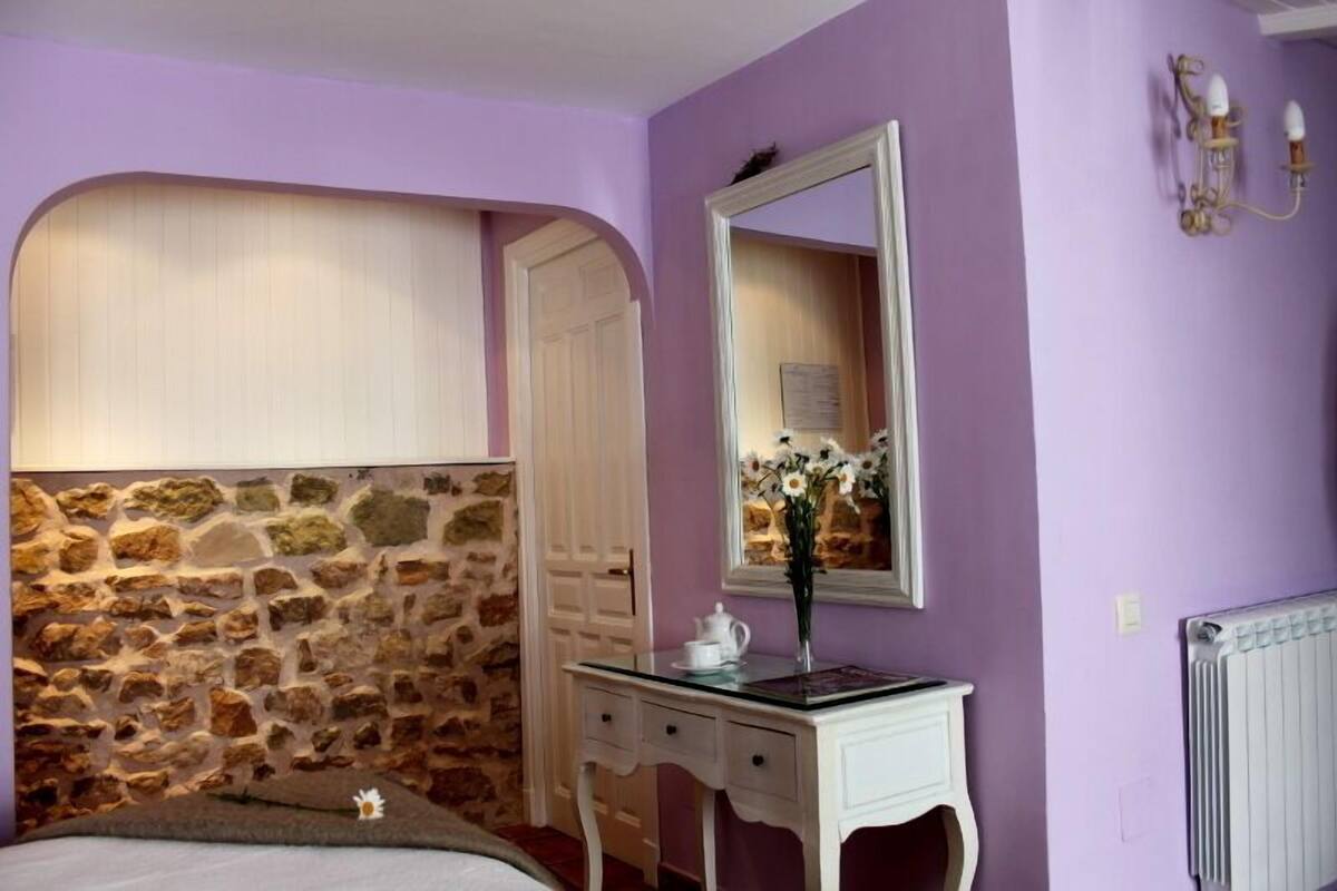 Een slaapkamer met een stenen muur, een witte deur, een dressoir, een spiegel en een radiator.