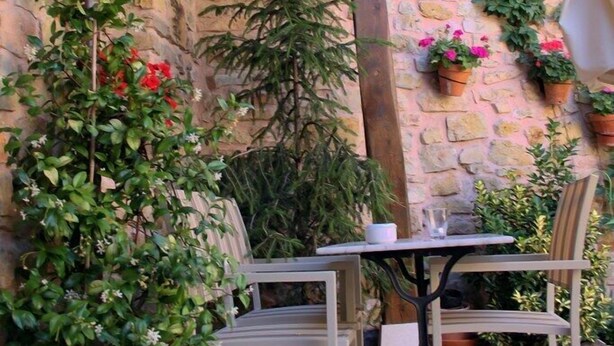 Eine Terrasse im Freien mit Steinmauern, Topfpflanzen und einem Tisch mit Stühlen.
