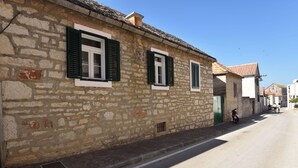 A stone building with green shutters and a narrow street. - Apartment Varos 1 (Primosten)