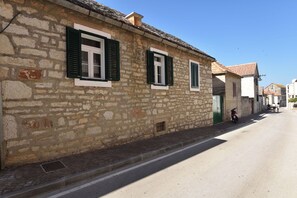 Ein Steinhaus mit grünen Fensterläden, eine schmale Straße und ein abgestellter Roller.