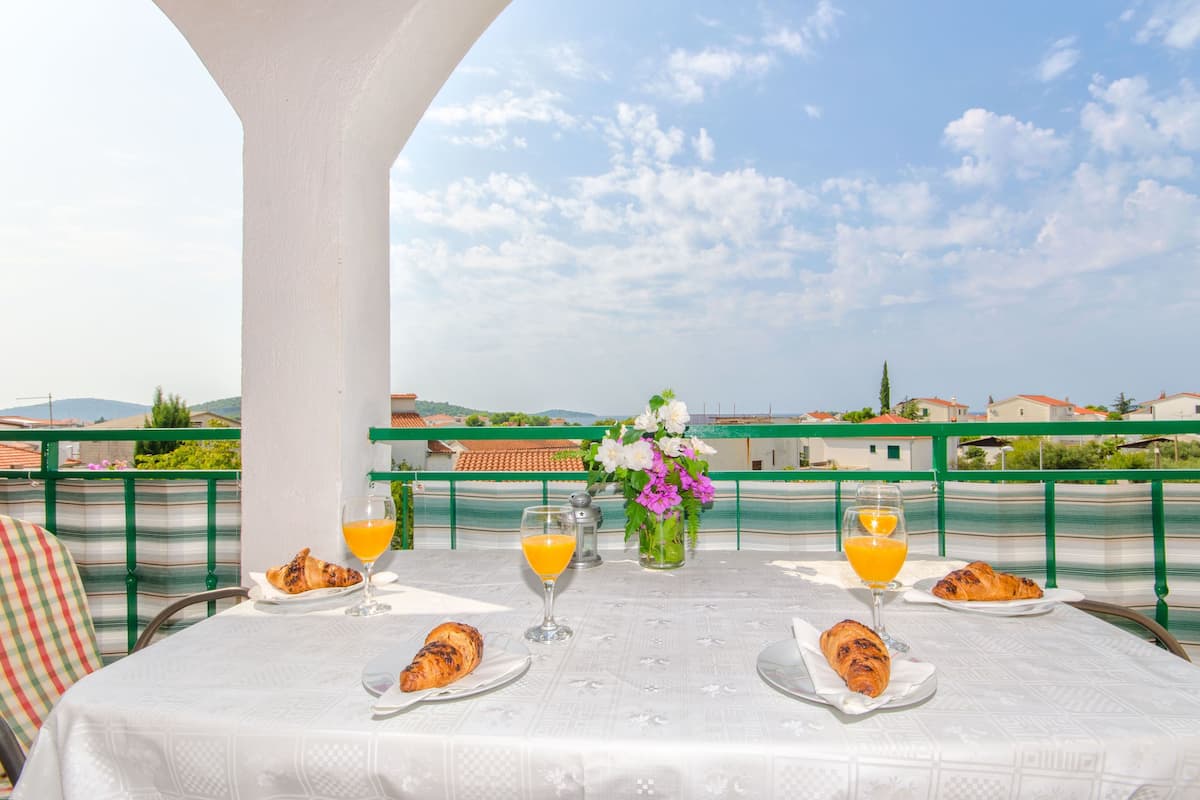 A table set with croissants and orange juice glasses, overlooking a scenic view with buildings and greenery.