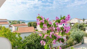 A balcony with a view of a coastal town, including houses with red-tiled roofs and a clear sky. - Apartments Zoric (Rogoznica)