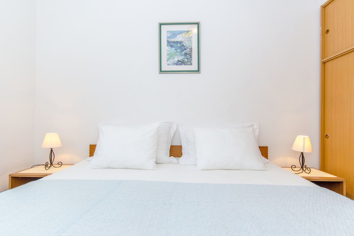 A neatly made bed with white linens, two bedside lamps, and a framed picture on the wall.