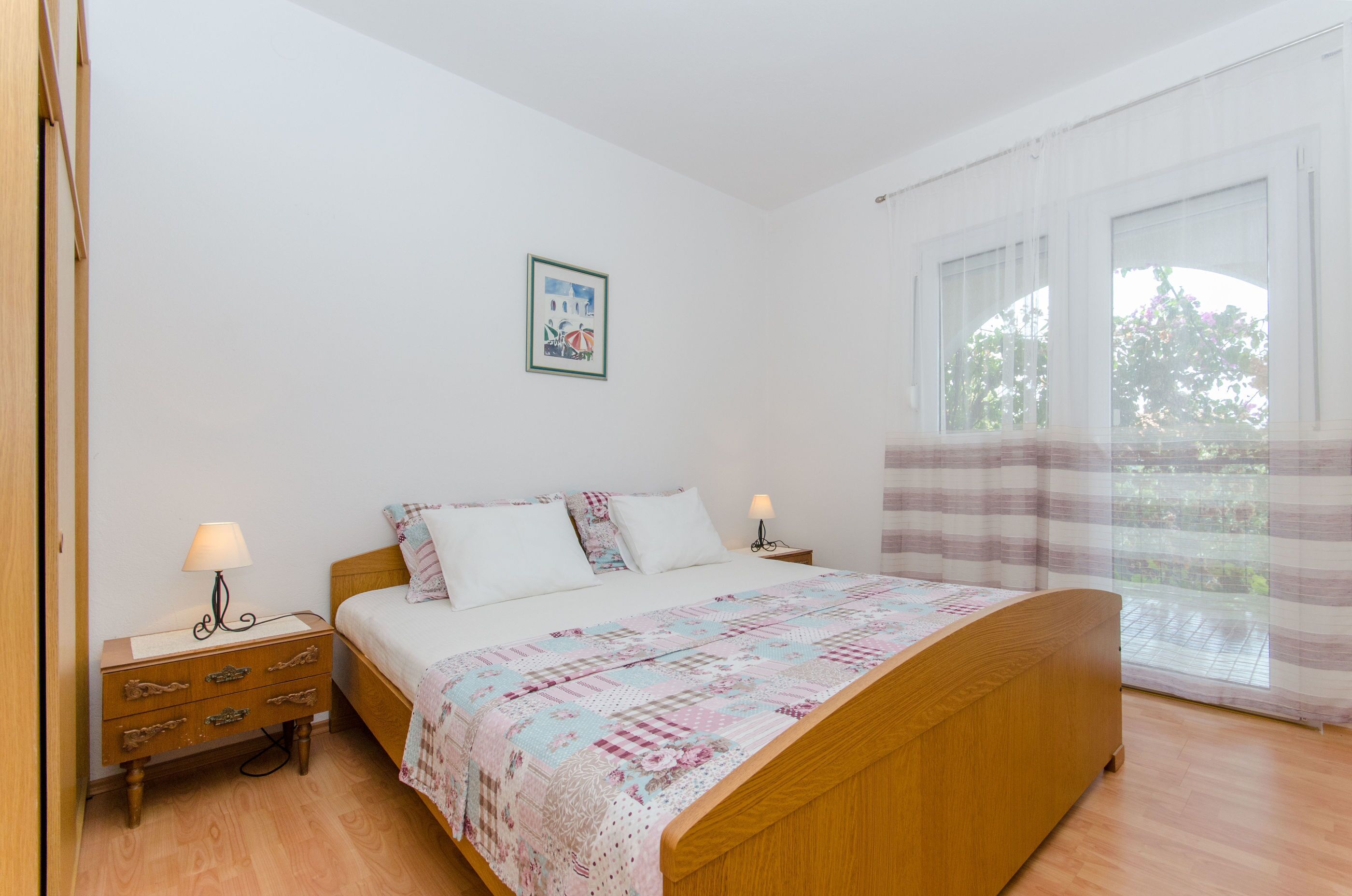 Une chambre à coucher avec un lit en bois, deux tables de chevet, une commode, une fenêtre avec des rideaux et un tableau accroché au mur.