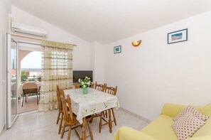 Un coin repas avec une table dressée pour quatre personnes, un canapé jaune et un téléviseur fixé au mur.