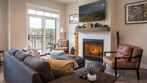 A living room with a fireplace, a sofa, a chair, and a television on the wall. - Hideaway Station TS 23 - Downtown Winter Park (Winter Park)