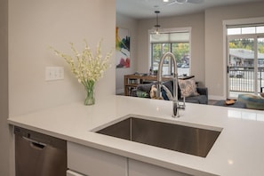 A modern kitchen with a stainless steel sink, a dishwasher, and a vase of flowers on the counter.
