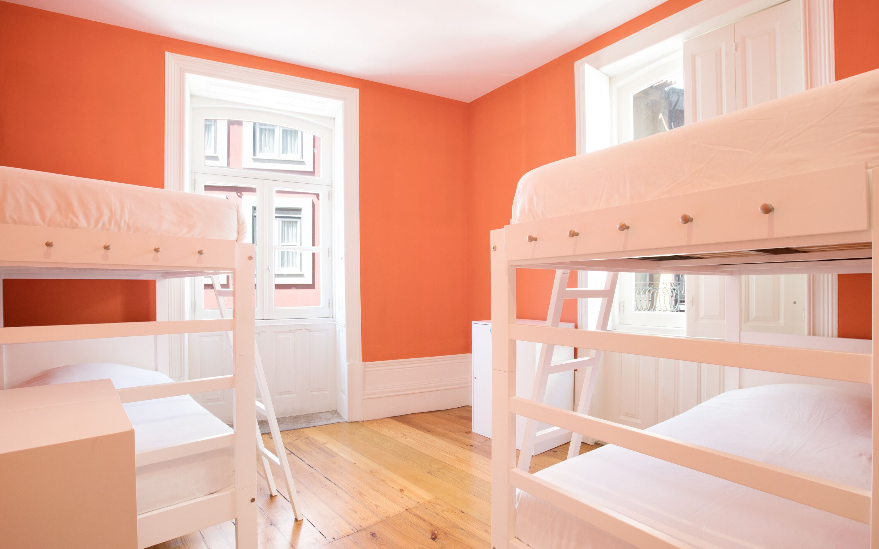A room with two bunk beds, wooden flooring, and orange walls.