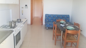 Una cocina compacta con estufa a gas, horno y un área de comedor con mesa, sillas y un sofá estampado.