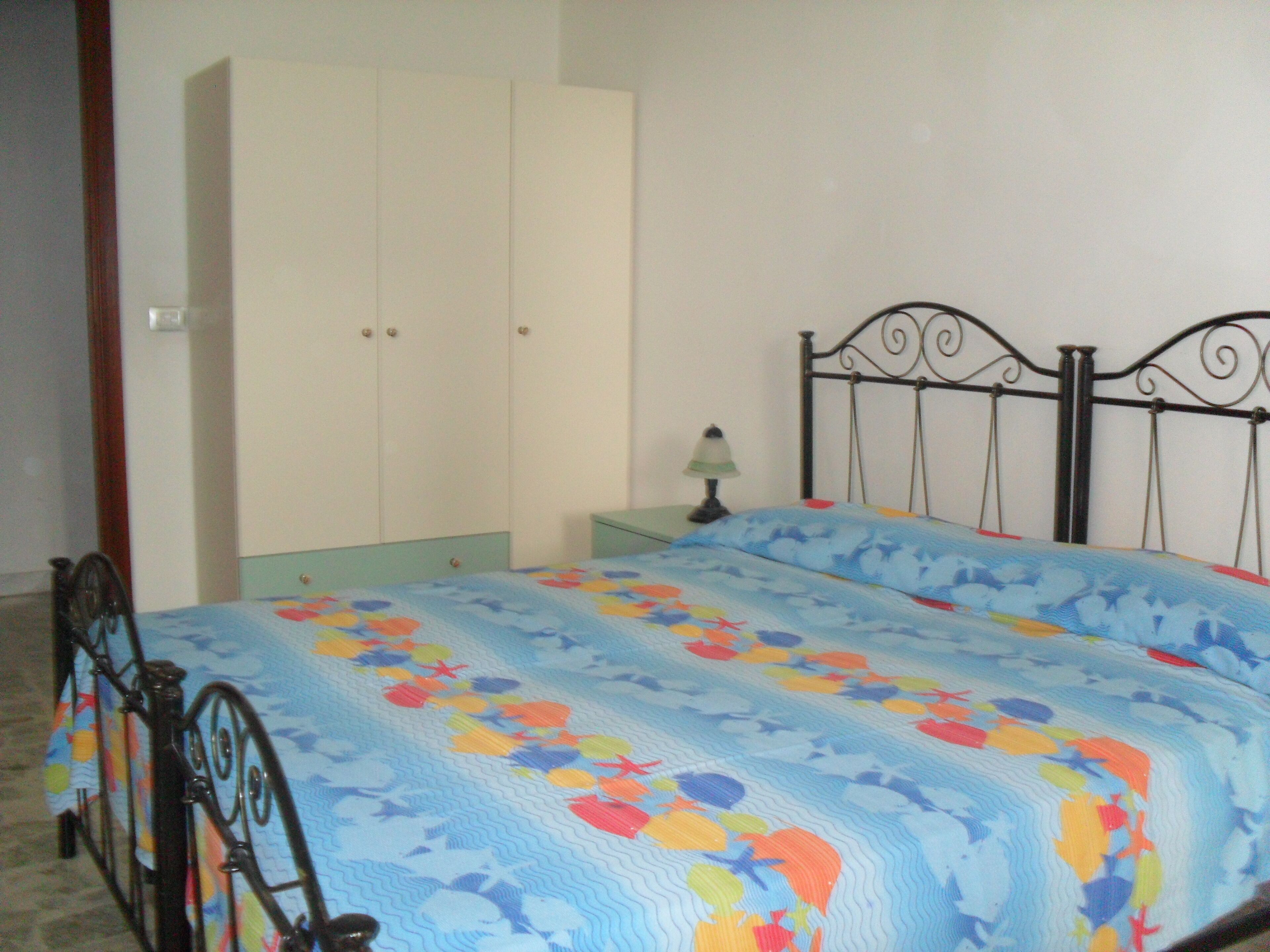 Un dormitorio con cama, armario, mesita de noche y lámpara.