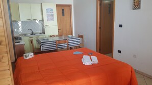 Una habitación con una cama, una mesa de comedor con sillas, una zona de cocina y una puerta que da a otra habitación.
