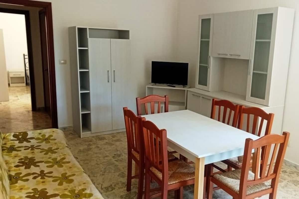 A dining area with a table and chairs, a television on a stand, and cabinets against the wall.