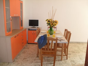A dining area with a table set for four, a television, and a vase with sunflowers.