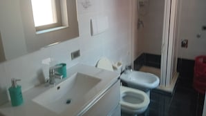 Un baño con un lavamanos, dos inodoros, una ducha y una ventana.