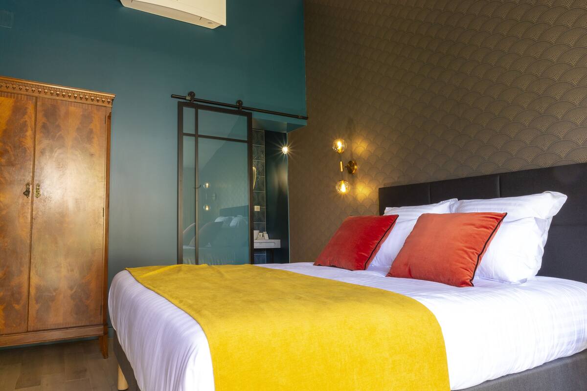 Une chambre d’hôtel avec un grand lit, une armoire et une salle de bain visible à travers une porte en verre.