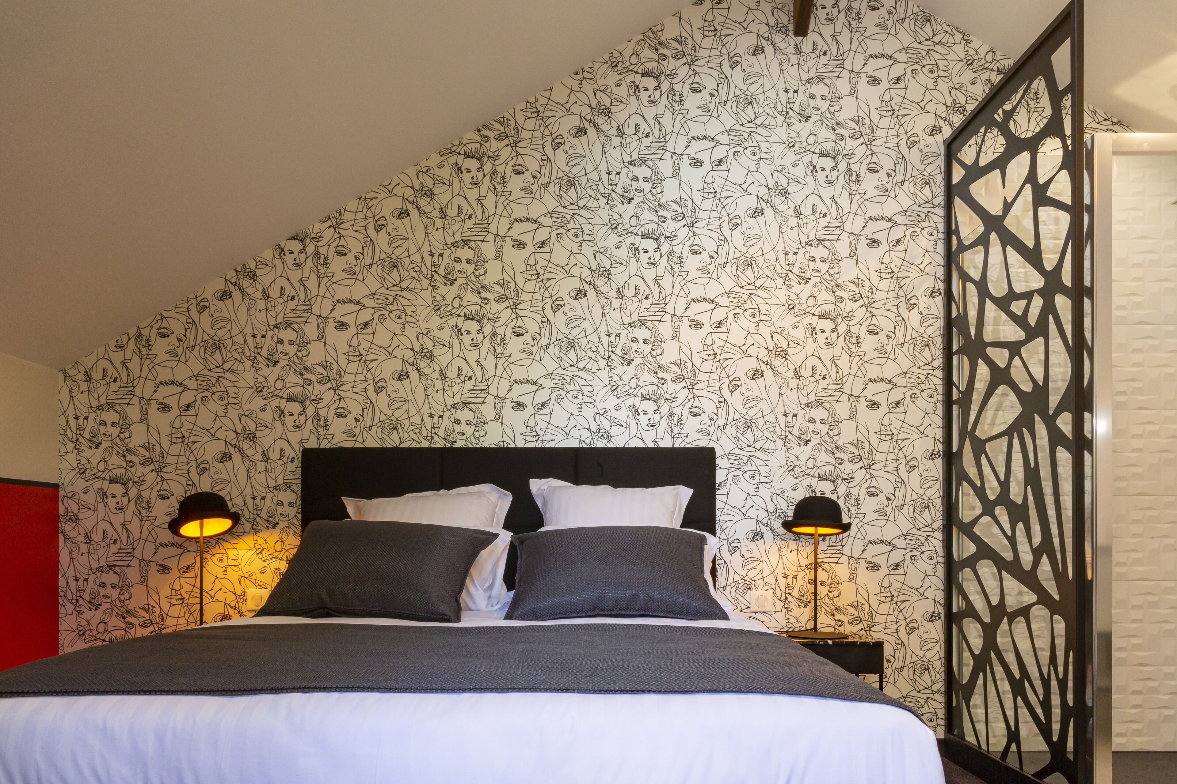 A neatly made bed with a black headboard, two bedside lamps, and a patterned wallpaper.
