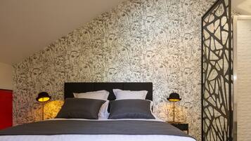 A neatly made bed with a black headboard, two bedside lamps, and a patterned wallpaper.