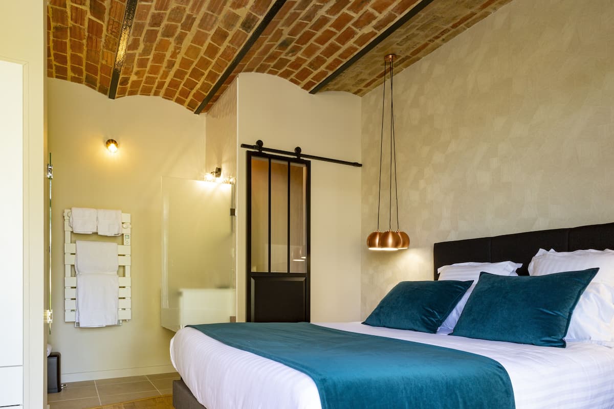 Une chambre d’hôtel avec un grand lit, une salle de bain équipée d’un porte-serviettes et un plafond en briques.