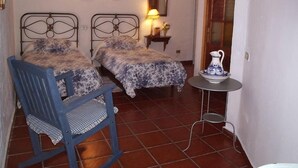 A room with two beds, a chair, a small table with a vase, and a wall-mounted mirror. - Casa Rural las Cáscaras (Tejeda)