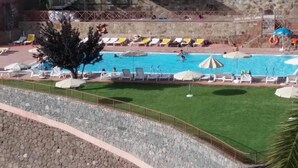 A pool area with lounge chairs and umbrellas, surrounded by a stone wall and a grassy area. - Casa Rural las Cáscaras (Tejeda)