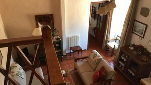 A cozy living room with a sofa, a wooden coffee table, and a dining table. A staircase leads to an upper floor, and a mirror reflects part of the room. - Casa Rural las Cáscaras (Tejeda)