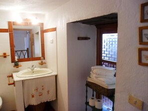 A bathroom with a sink, mirror, and towel rack. There is a window with a view of trees. - Casa Rural las Cáscaras (Tejeda)