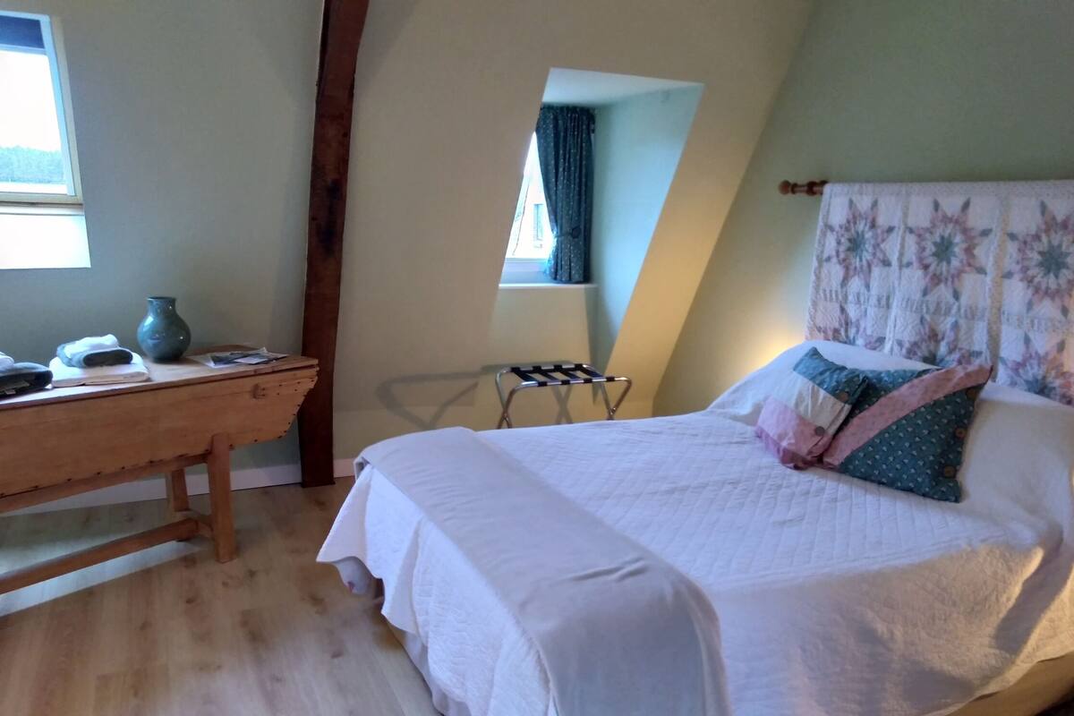 Une chambre à coucher avec un lit, un bureau en bois, une chaise et une fenêtre.