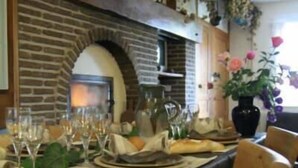 Un coin repas avec une cheminée en briques, une table dressée pour le repas et une plante en pot sur la droite.