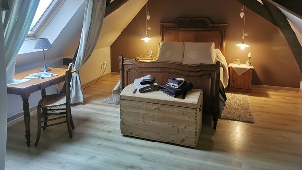 Une chambre mansardée chaleureuse, avec un plafond en pente, un bureau en bois, un lit avec une tête de lit et deux tables de chevet avec des lampes.