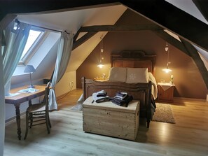 Une chambre mansardée chaleureuse, avec un plafond en pente, un bureau en bois, un lit avec une tête de lit et deux tables de chevet avec des lampes.