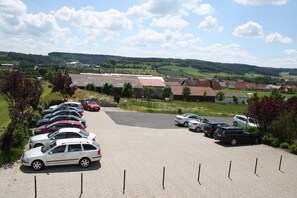 A parking lot with multiple cars and a view of a town with buildings and green hills in the background.