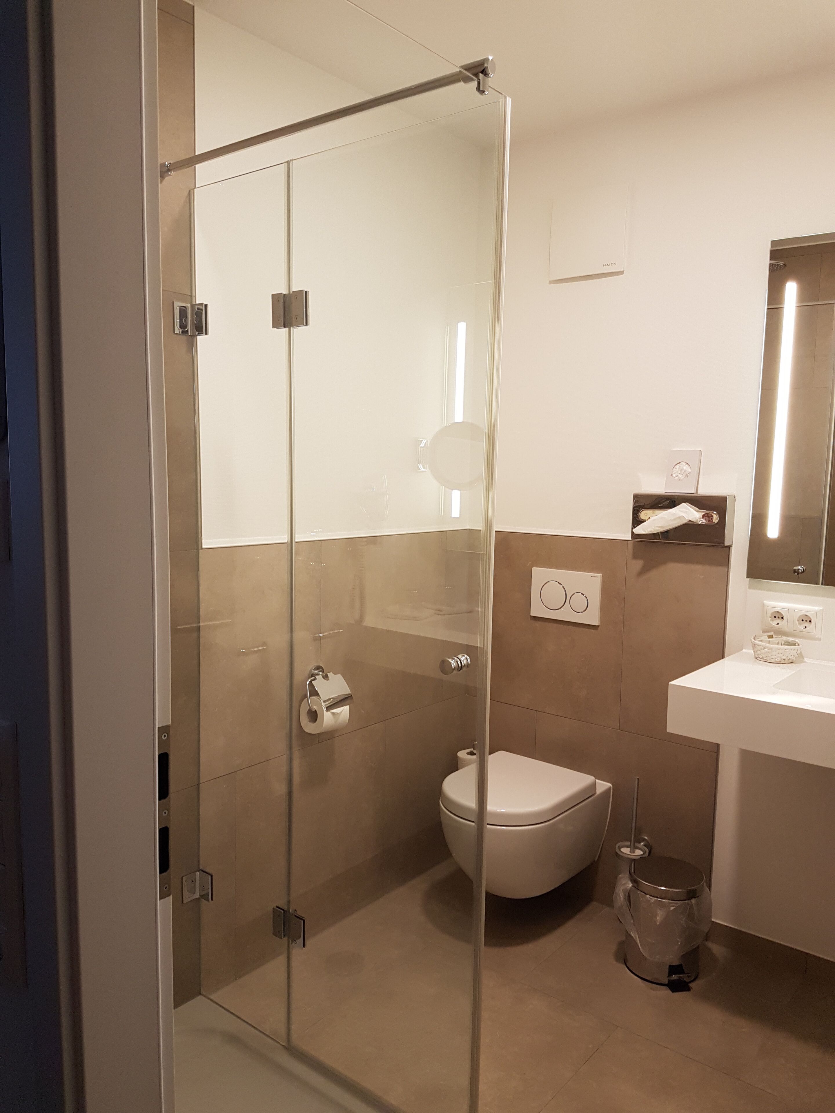 Un bagno moderno con box doccia in vetro, un water, un lavandino con specchio e un cestino.