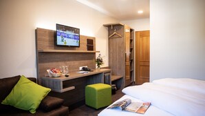 Una habitación de hotel con cama, escritorio con televisor, armario y reposapiés verde.