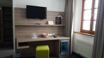 A hotel room with a wooden desk, a television, a radiator, and a window with curtains.