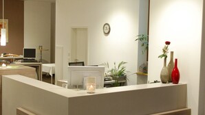Un área de recepción con mostrador, computadora, planta y jarra.