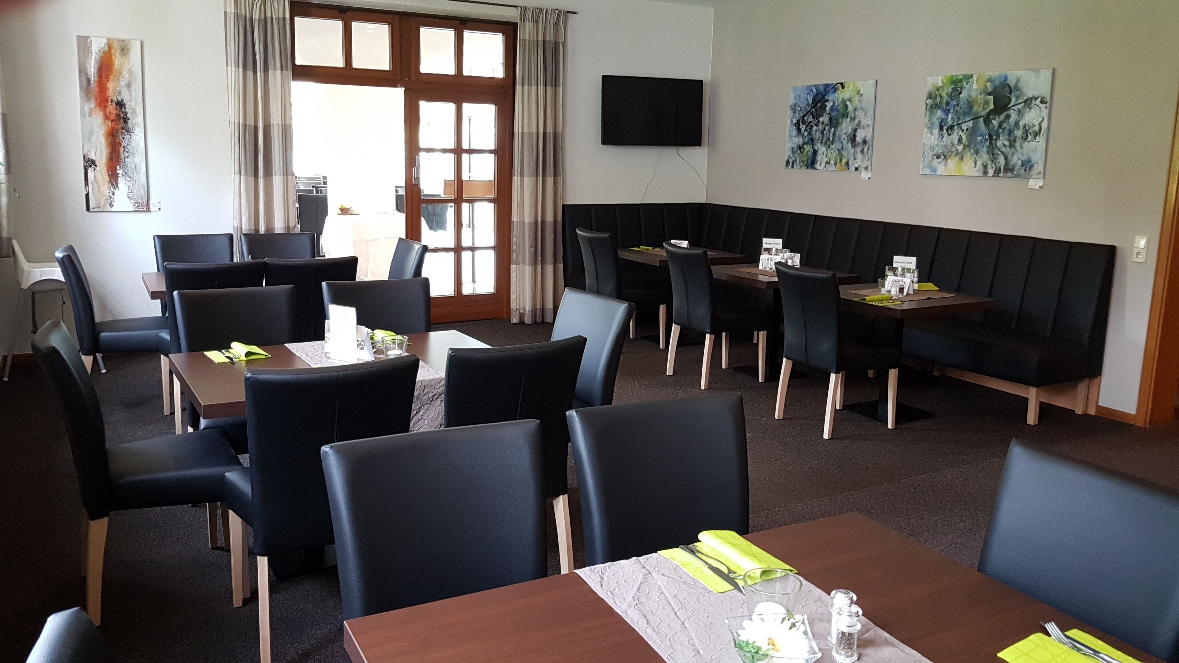 A dining area with tables and chairs, a television on the wall, and artwork on the walls.