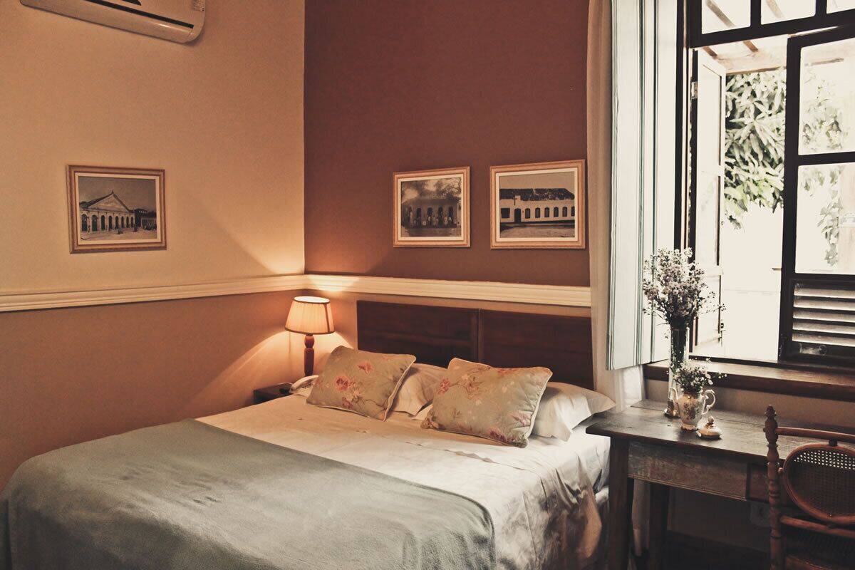 A neatly made bed with floral pillows, a bedside lamp, and framed pictures on the wall.