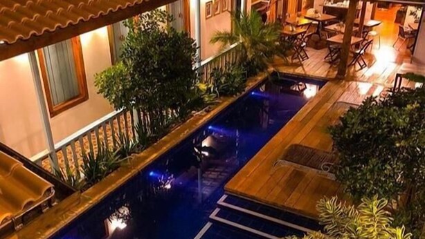 Un área de piscina en la azotea con terraza de madera, rodeada de abundante vegetación y un techo de tejas.