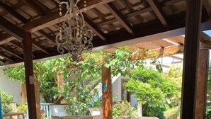 Un patio al aire libre con mesas de madera y sillas blancas, rodeado de exuberante follaje y una piscina.