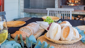 Une table dressée avec du pain, des raisins et un verre de vin, avec une cheminée et une enseigne « Guppy Huy's » en arrière-plan.