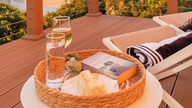 Un panier en osier contenant un verre d’eau, un livre et une miche de pain, posés sur une table, avec une vue panoramique en toile de fond.