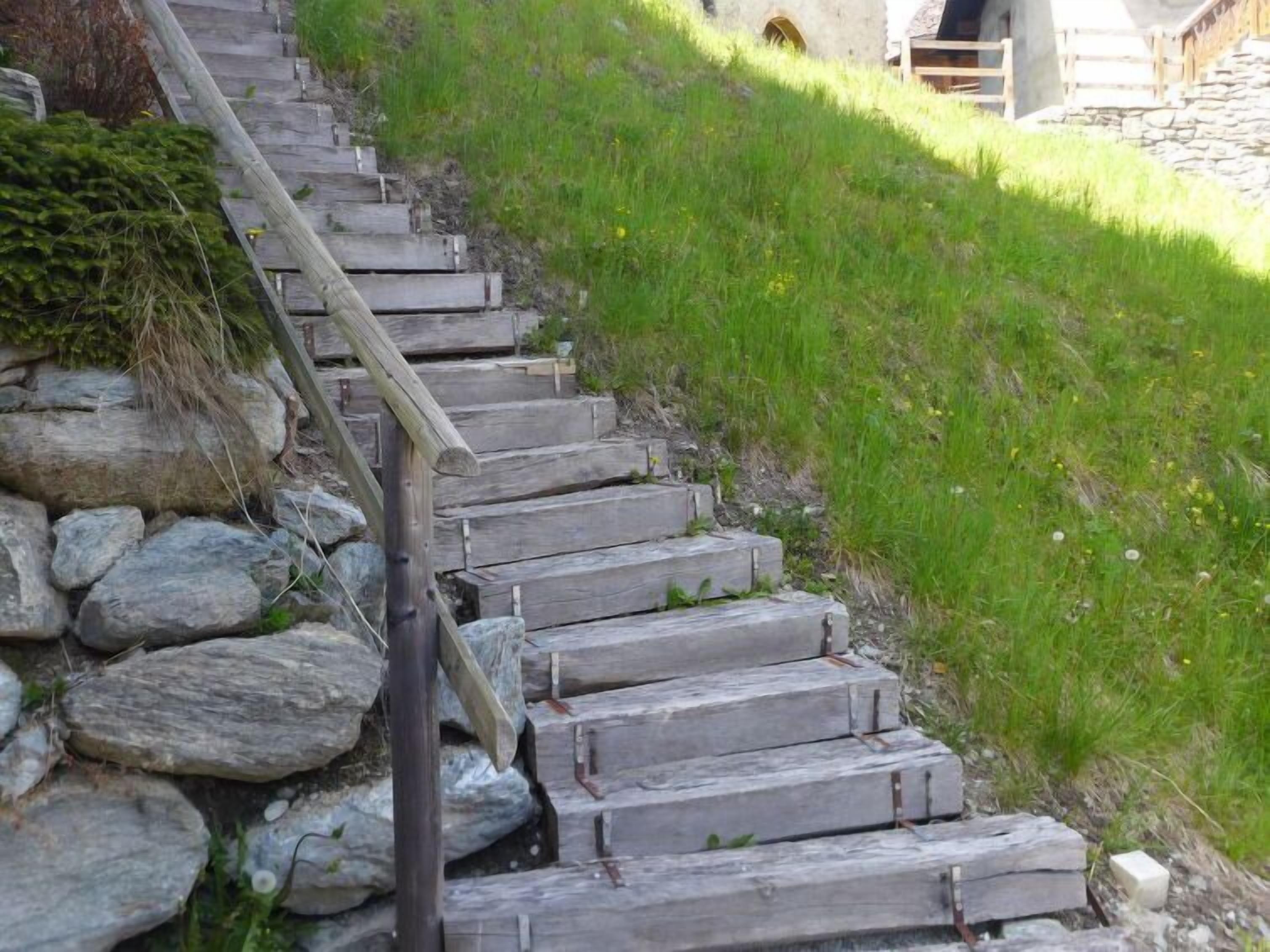 Eine Holztreppe mit Steinstufen, die einen grasbewachsenen Hang hinaufführt.