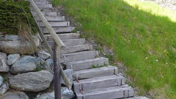 Eine Holztreppe mit Steinstufen, die einen grasbewachsenen Hang hinaufführt.