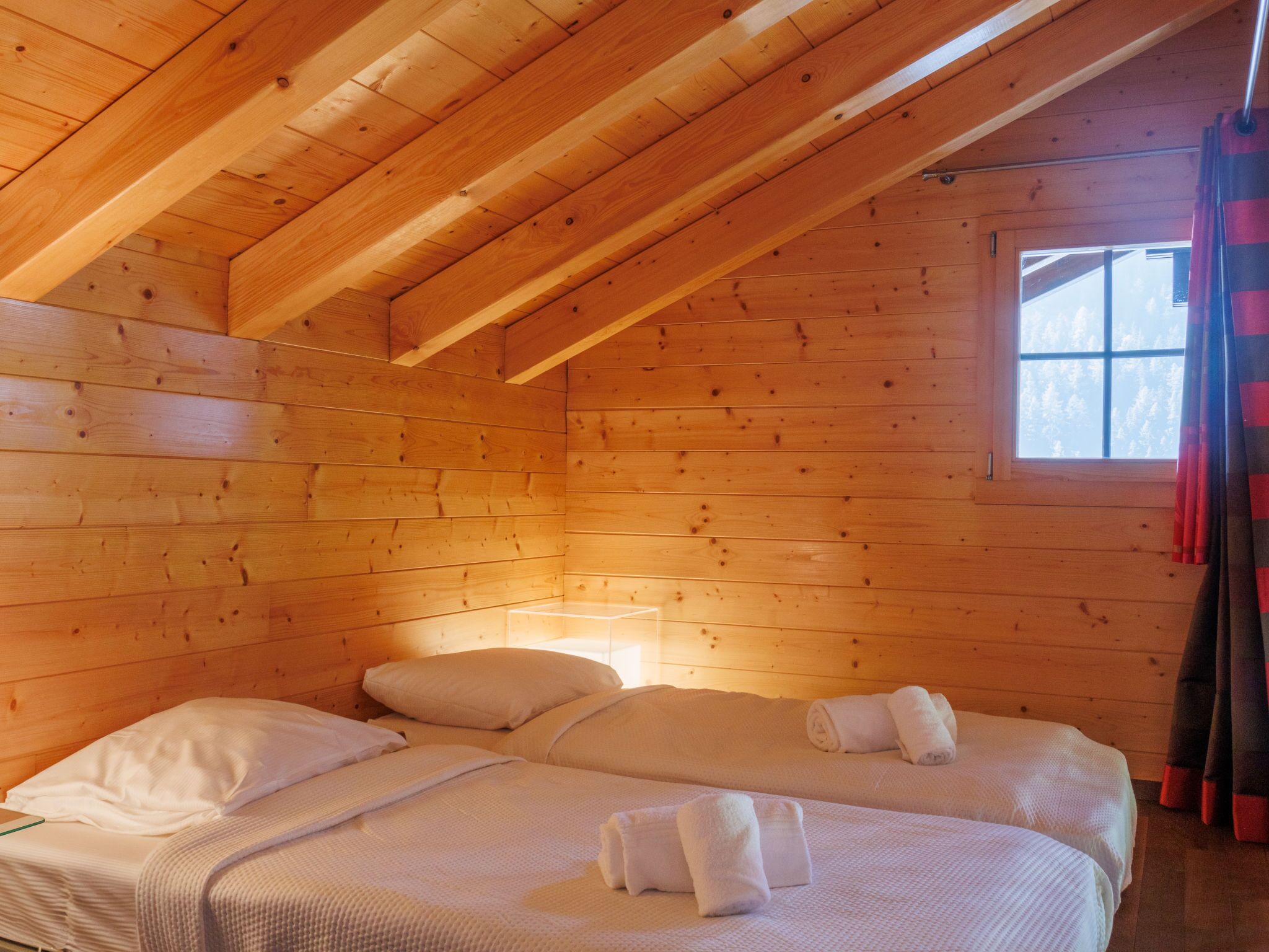 Une chambre confortable de style cabane, avec deux lits, des murs en bois et un plafond en pente.
