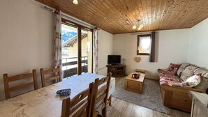 A cozy room with a wooden ceiling, a dining table with chairs, a sofa, a TV, and a view of mountains through the window. - Yéti 6 n° 8: renovated apartment at Petit Chatel (Châtel)