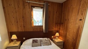 A bedroom with a wooden headboard, a large bed with a white quilt, two bedside tables with lamps, and a window with a curtain. - Yéti 6 n° 8: renovated apartment at Petit Chatel (Châtel)